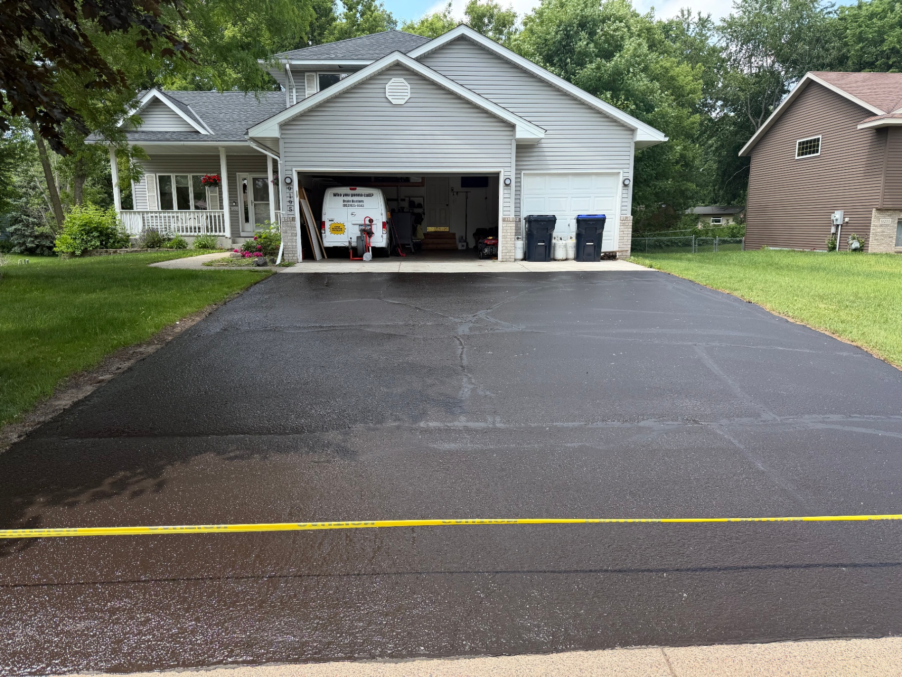 Freshly seal-coated residential driveway in front of a gray home