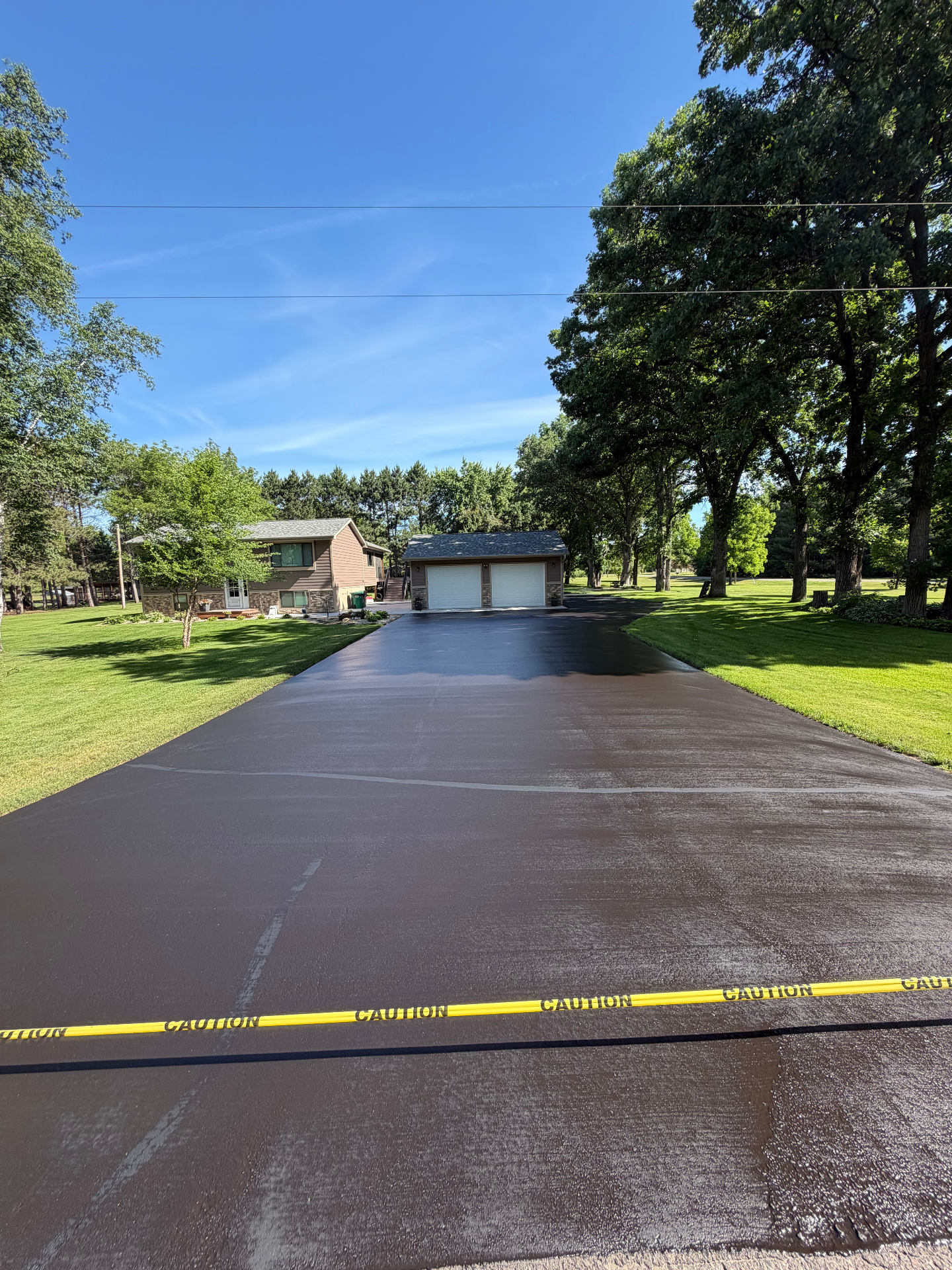 Freshly seal-coated driveway with caution tape in front of a Minnesota home