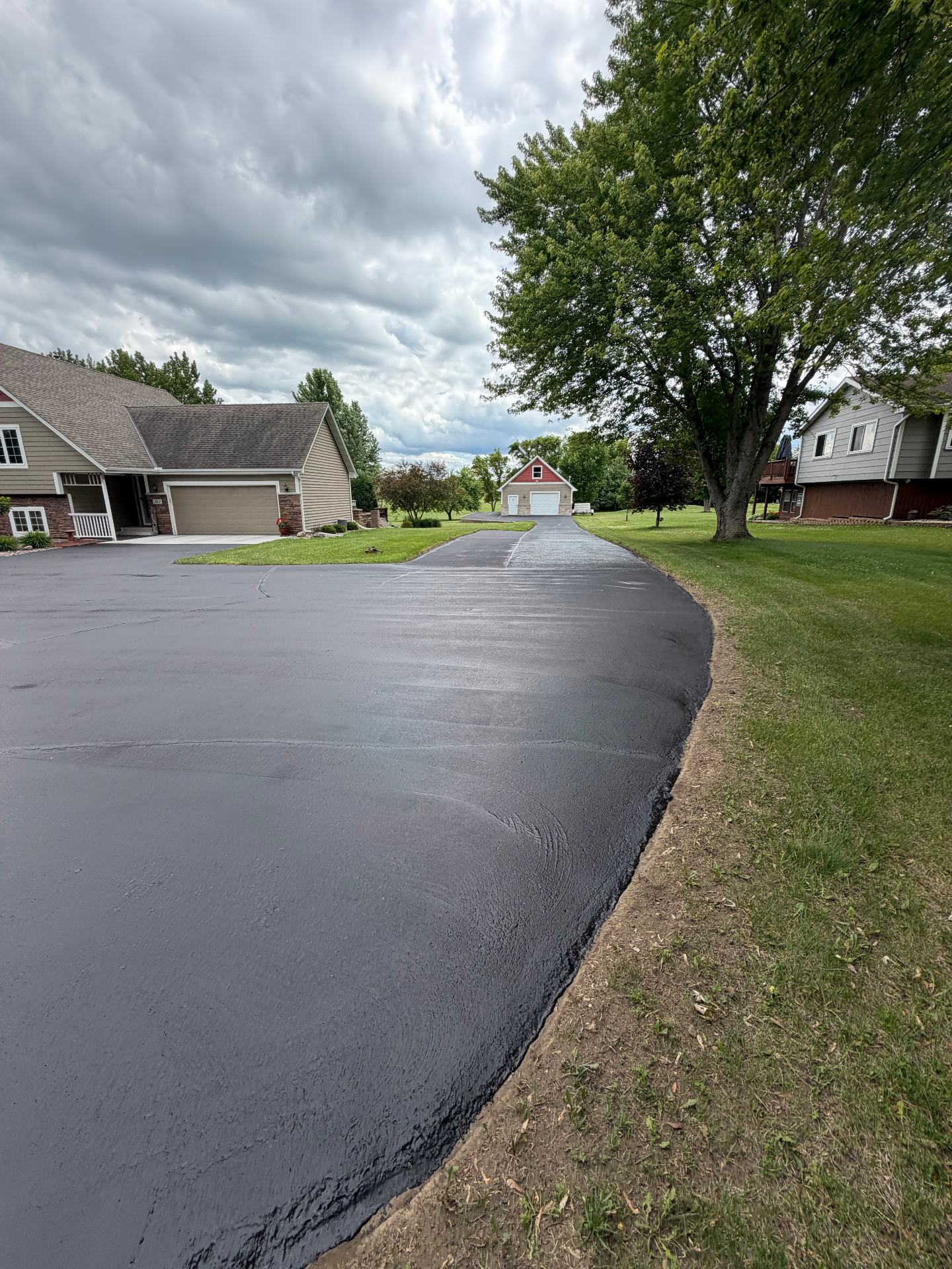 Wide residential driveway with a deep black seal coat finish under cloudy skies