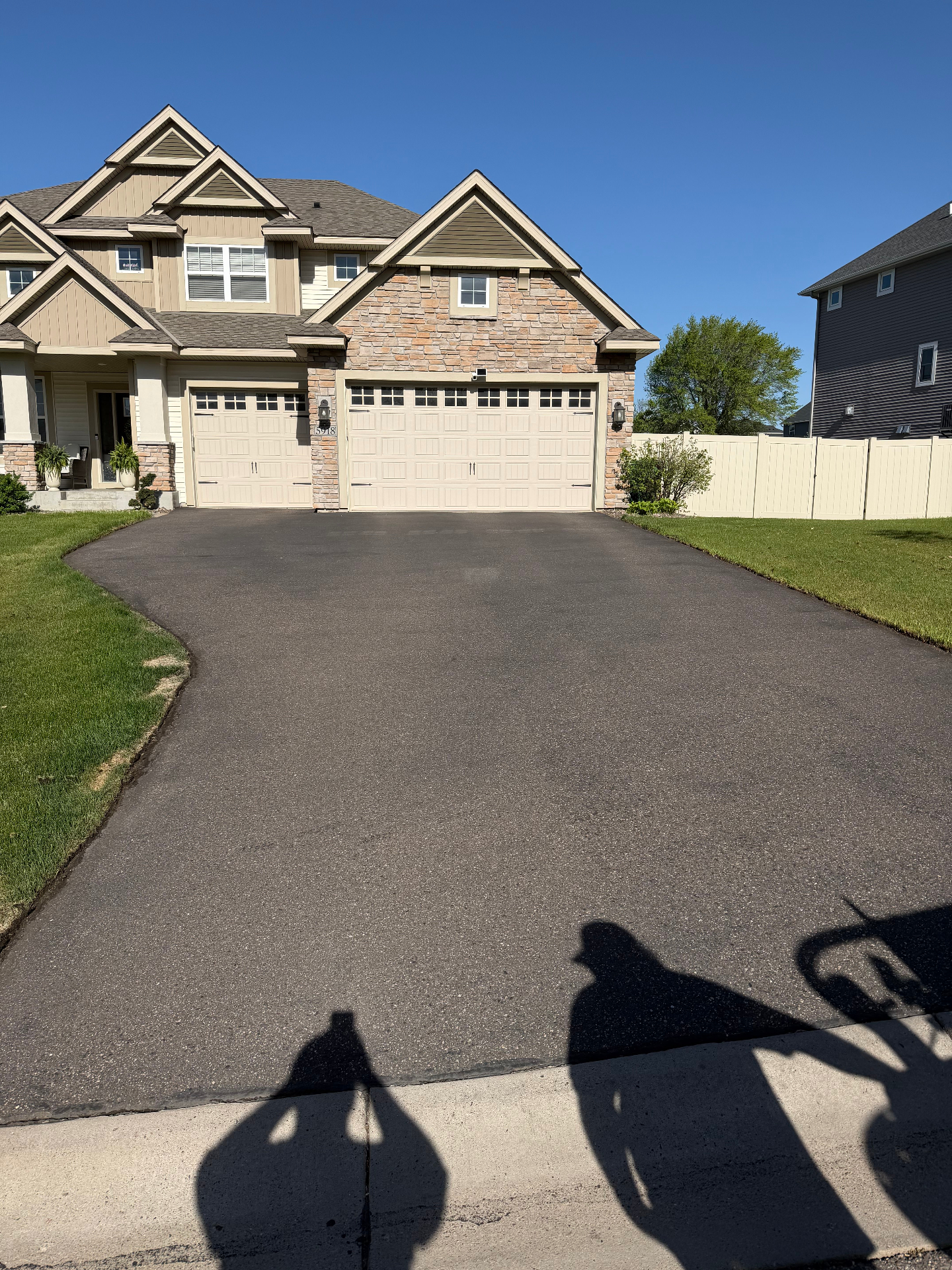 Wide three-car driveway leading to a stone-accent two-story home after seal coating