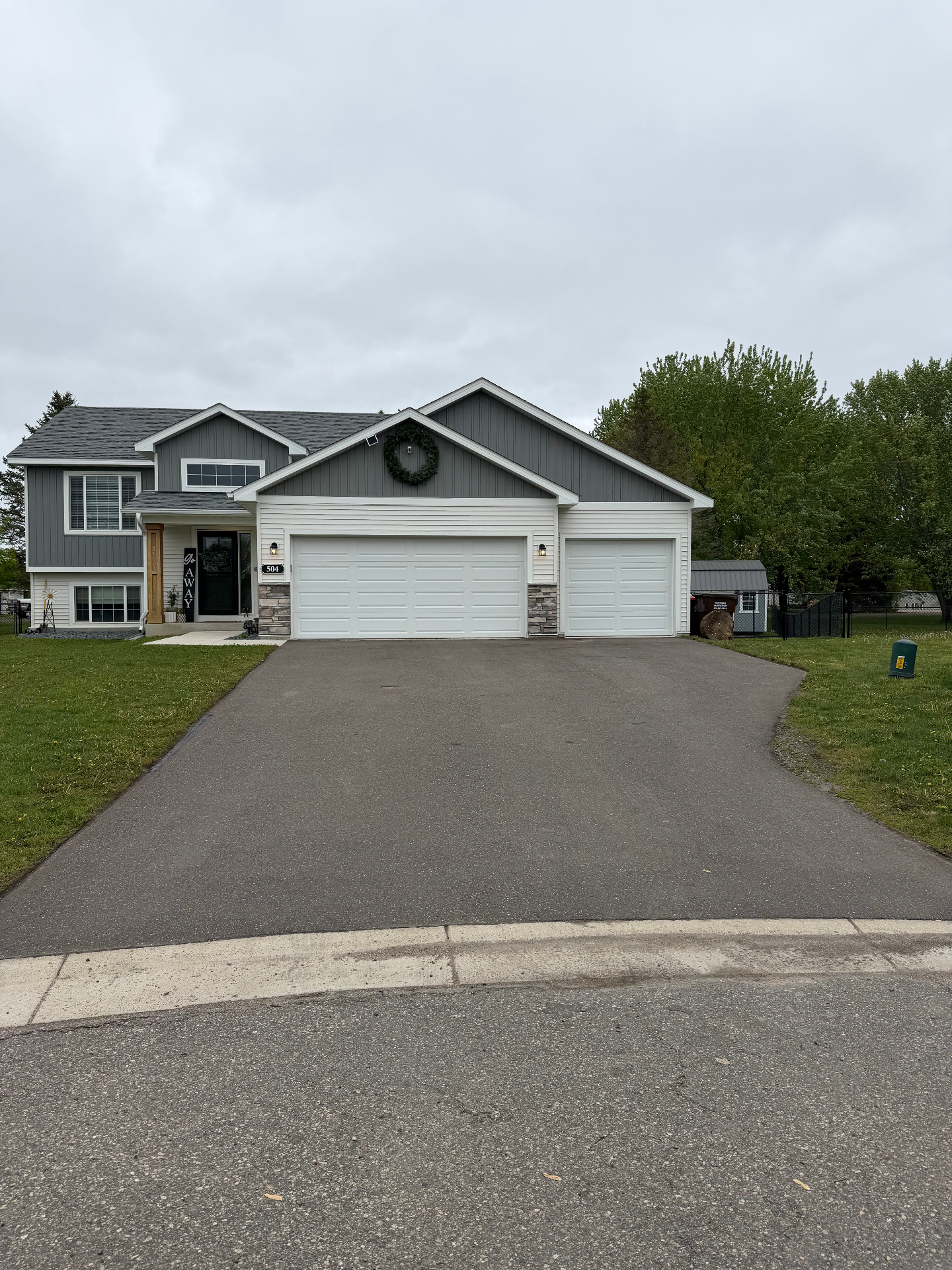 Freshly sealed residential driveway in front of a gray split-level home with a clean, even finish